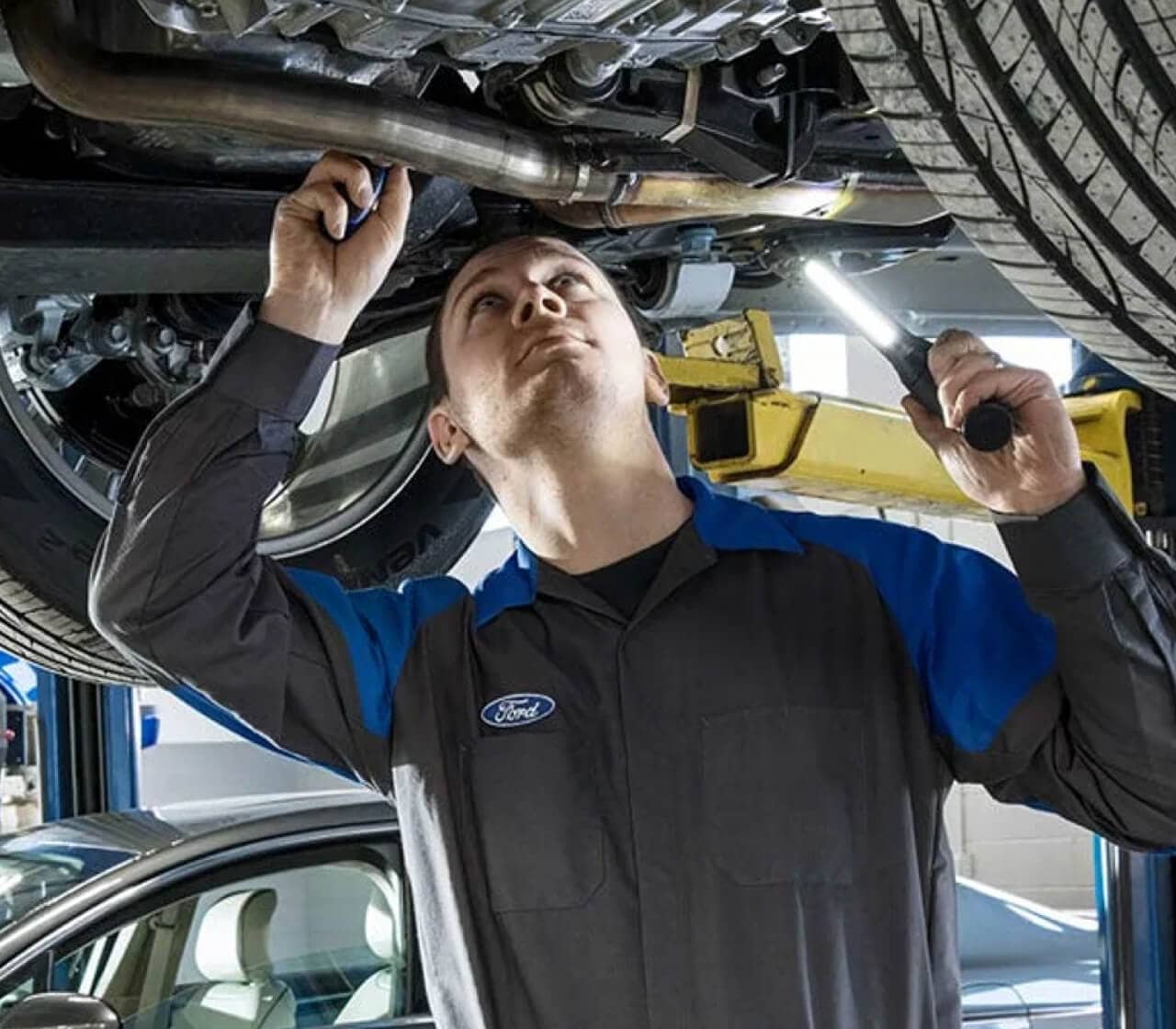 Ford Service Technician looking at the exhaust of a Ford Vehicle with a flashlight