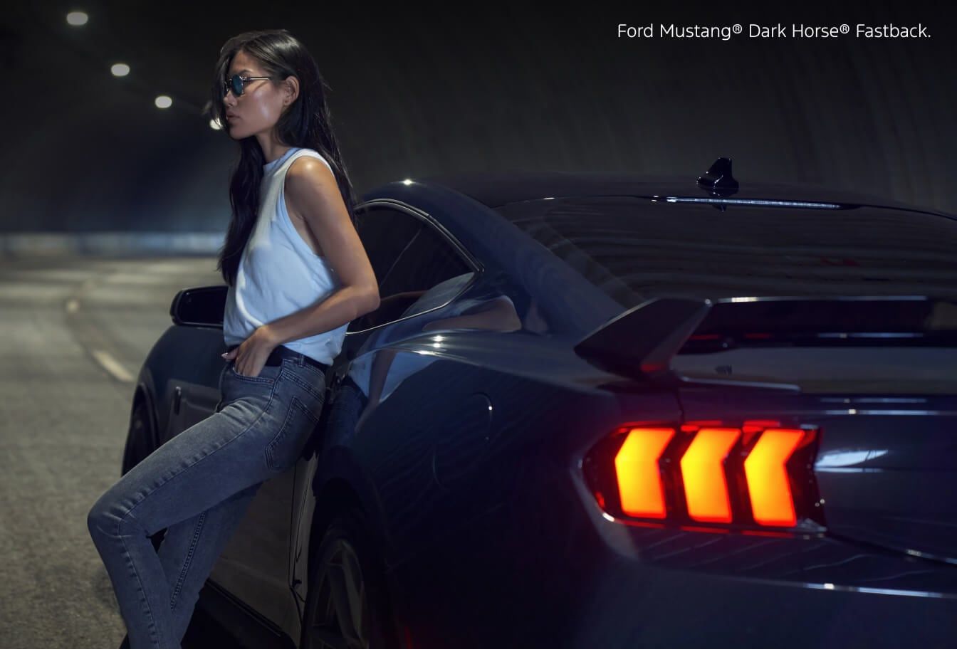 Side three-quarter view of a 2026 Blue Ford Mustang Dark Horse Fastback parked inside a tunnel next to a standing model.