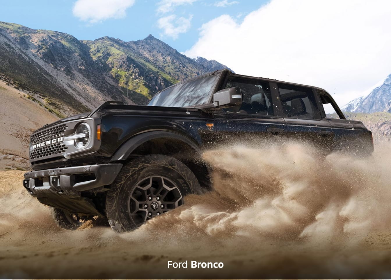 A black 2026 Ford Bronco Badlands kicking up sand in front of a mountainous backdrop
