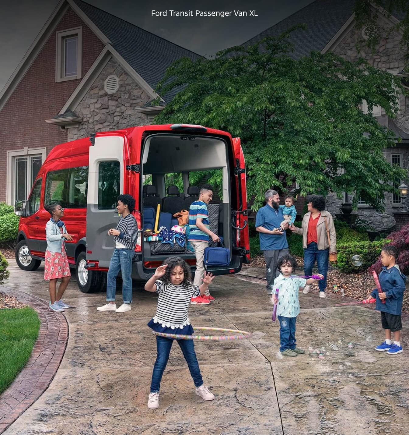 Three-quarter rear view of a 2027 Ford Transit Passenger Van XL in Race Red parked on a paved driveway in front of a stone house.