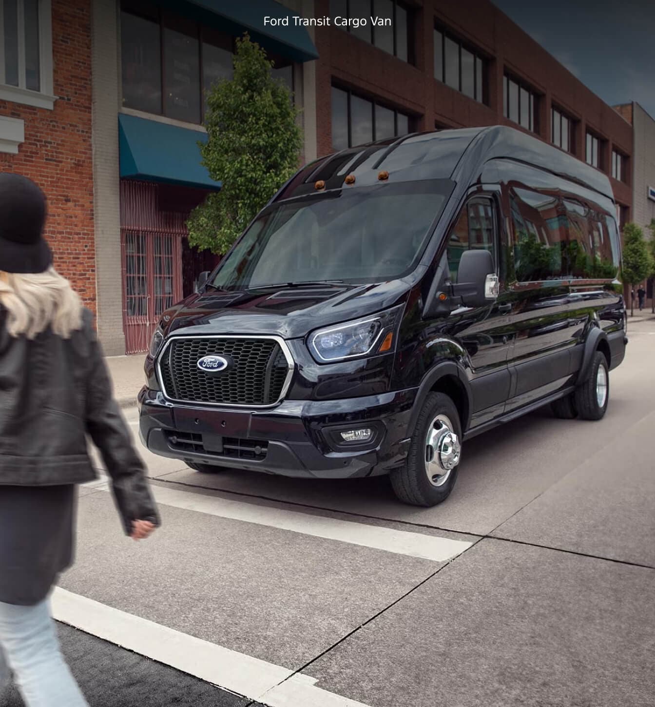 Front three-quarter view of a 2027 Ford Transit Cargo Van in Agate Black Metallic driving through a downtown street.
