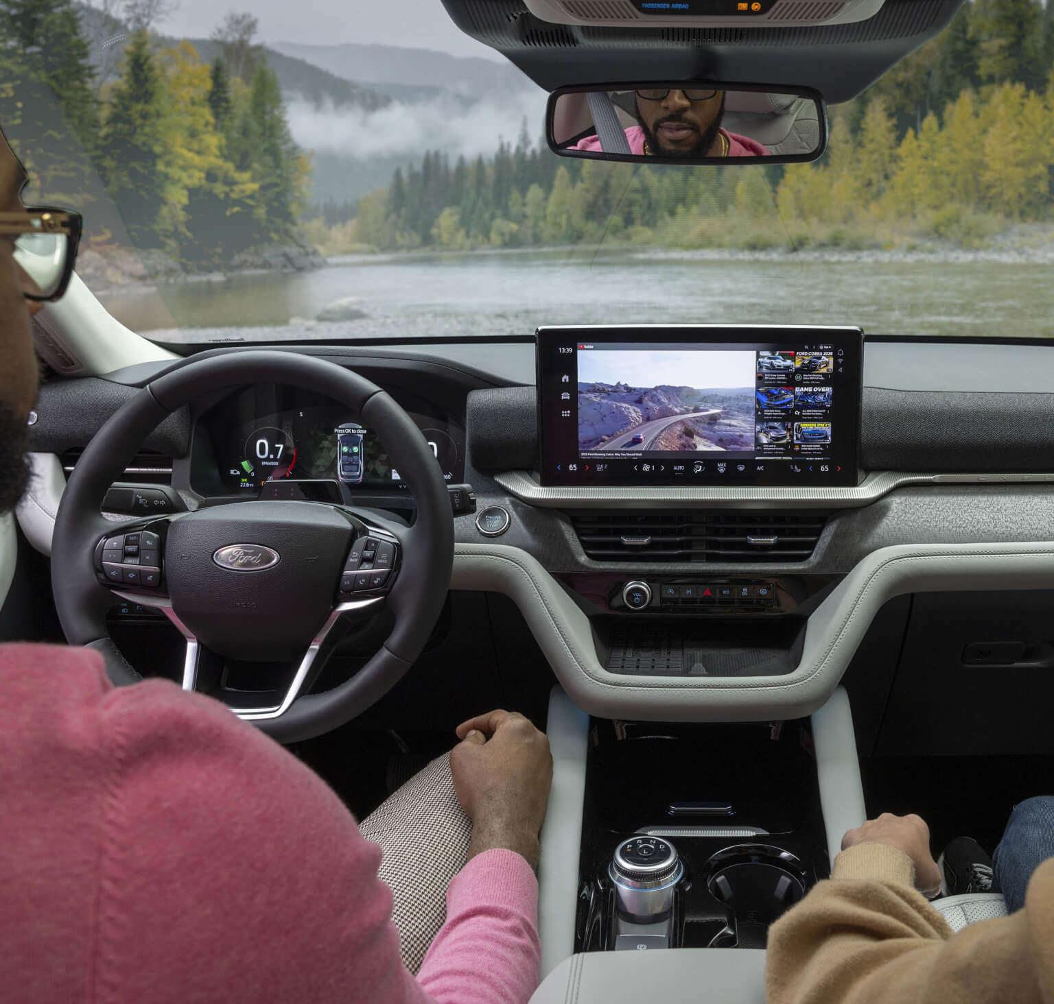Two people in the front seat of a 2026 Ford Explorer as they are parked looking out over a river and forest terrain