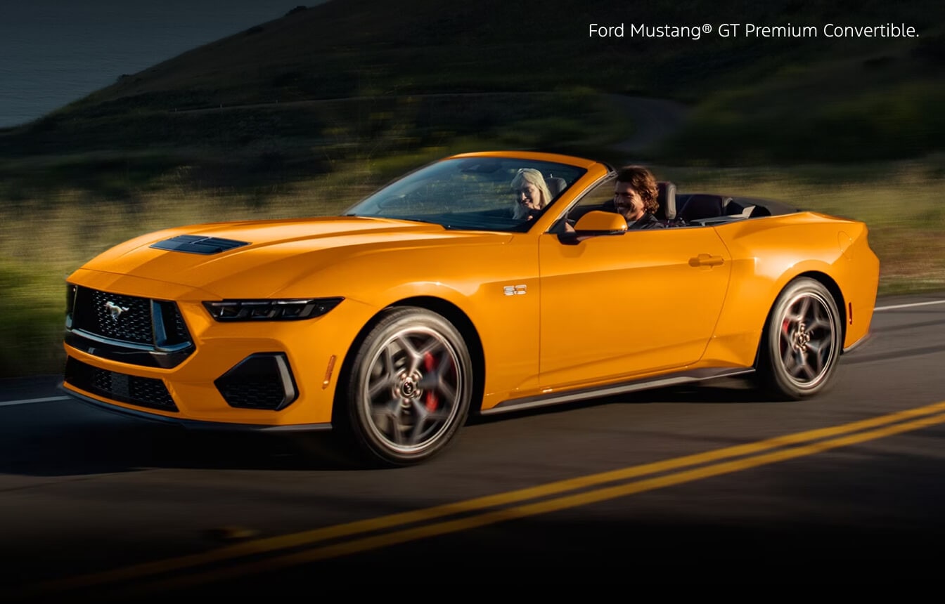 Front three-quarter view of a 2026 Yellow Ford Mustang GT Premium Convertible cruising on a coastal highway.