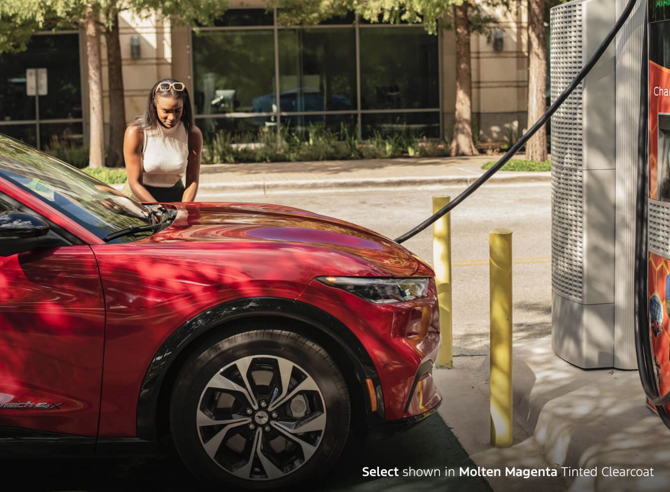 Mustang Mach E Select in Molten Magenta Tinted Clearcut charging at an EV charging station in a parking lot