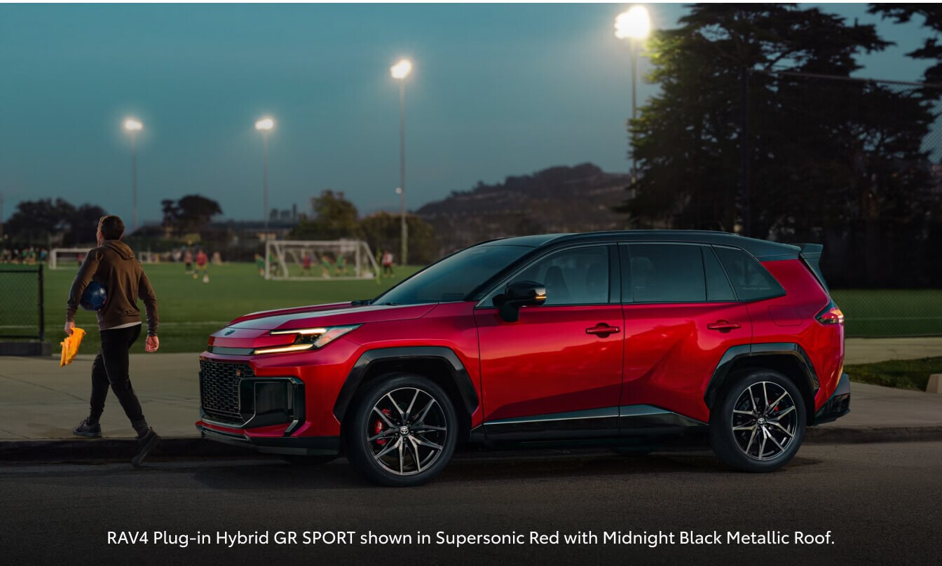Side profile view of a Supersonic Red Toyota RAV4 Plug-In Hybrid GR Sport parked at dusk next to a soccer field.