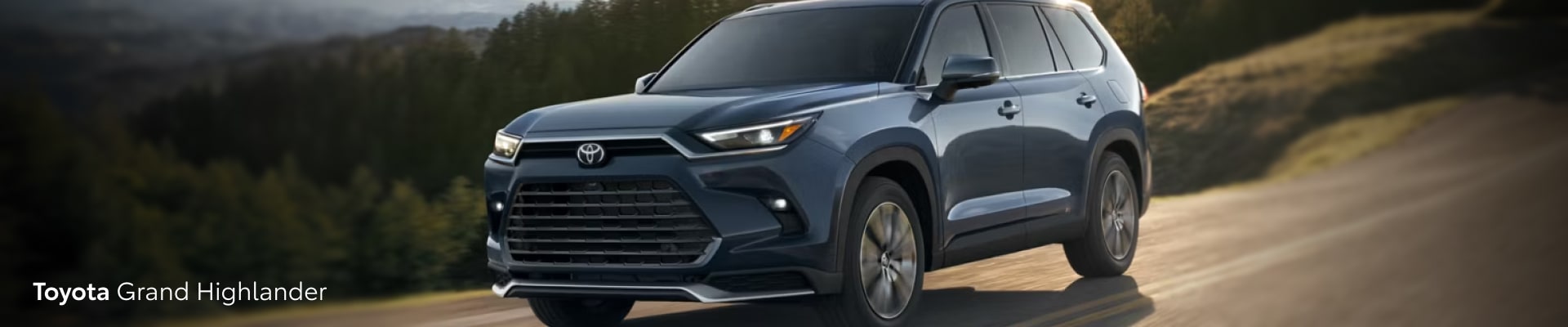 2026 Toyota Grand Highlander in blue driving with evergreen trees in the background