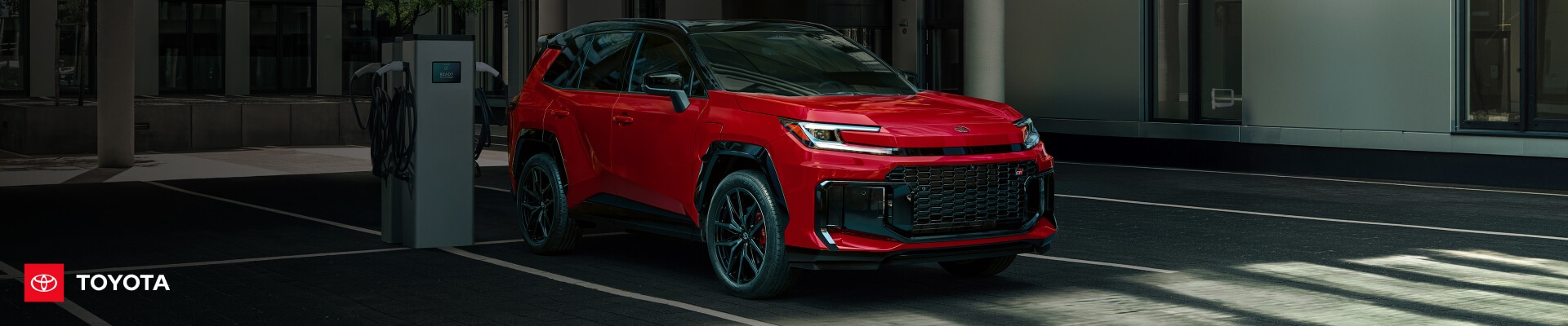 Front three-quarter view of a Supersonic Red Toyota RAV4 Plug-In Hybrid GR Sport parked next to a public Level 2 charging station.