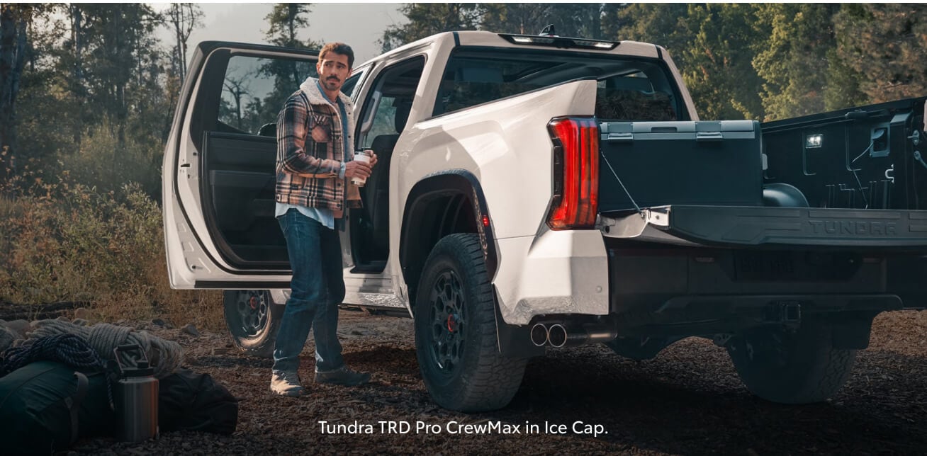 Rear three-quarter view of a white Toyota Tundra TRD Pro with an open door and tailgate at a campsite.