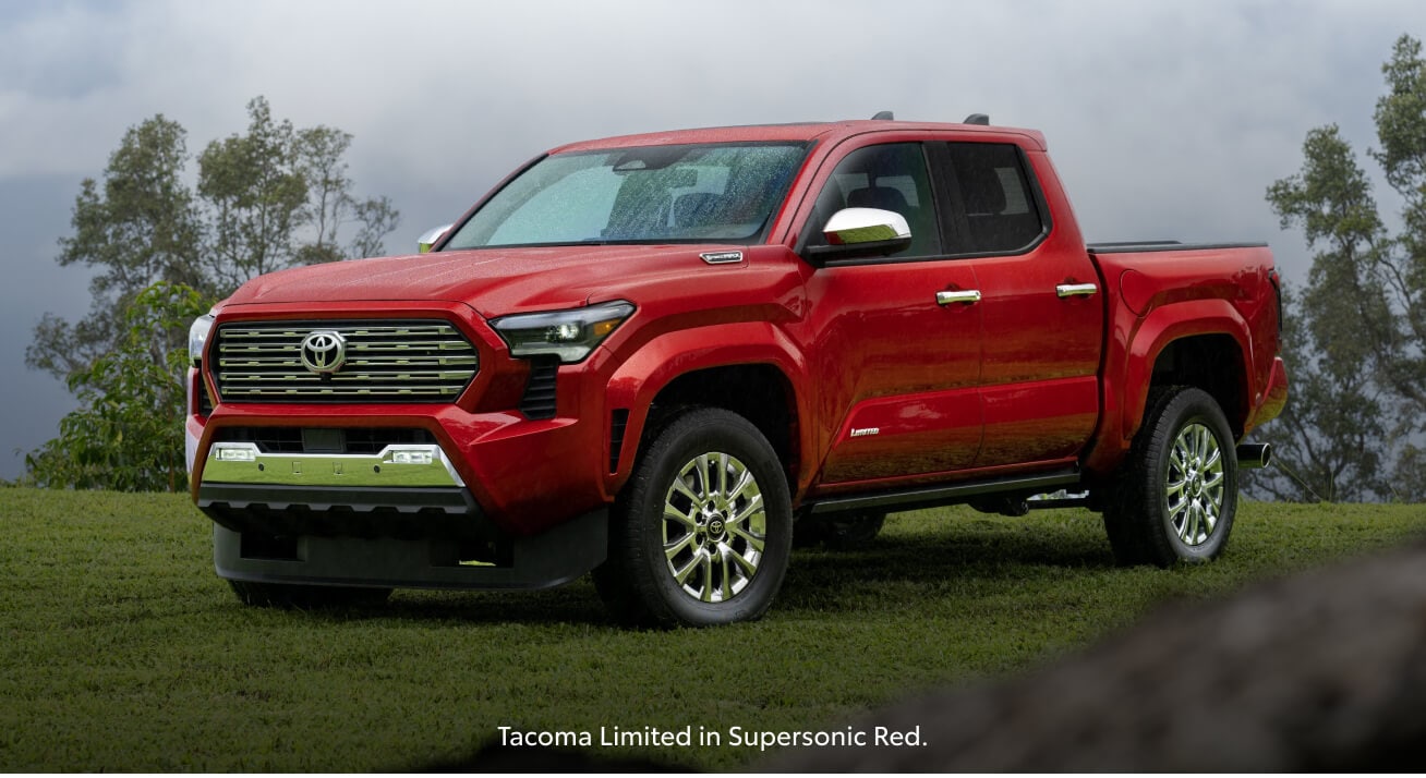 Front three-quarter view of a red Toyota Tacoma Limited parked on a green grassy hill.
