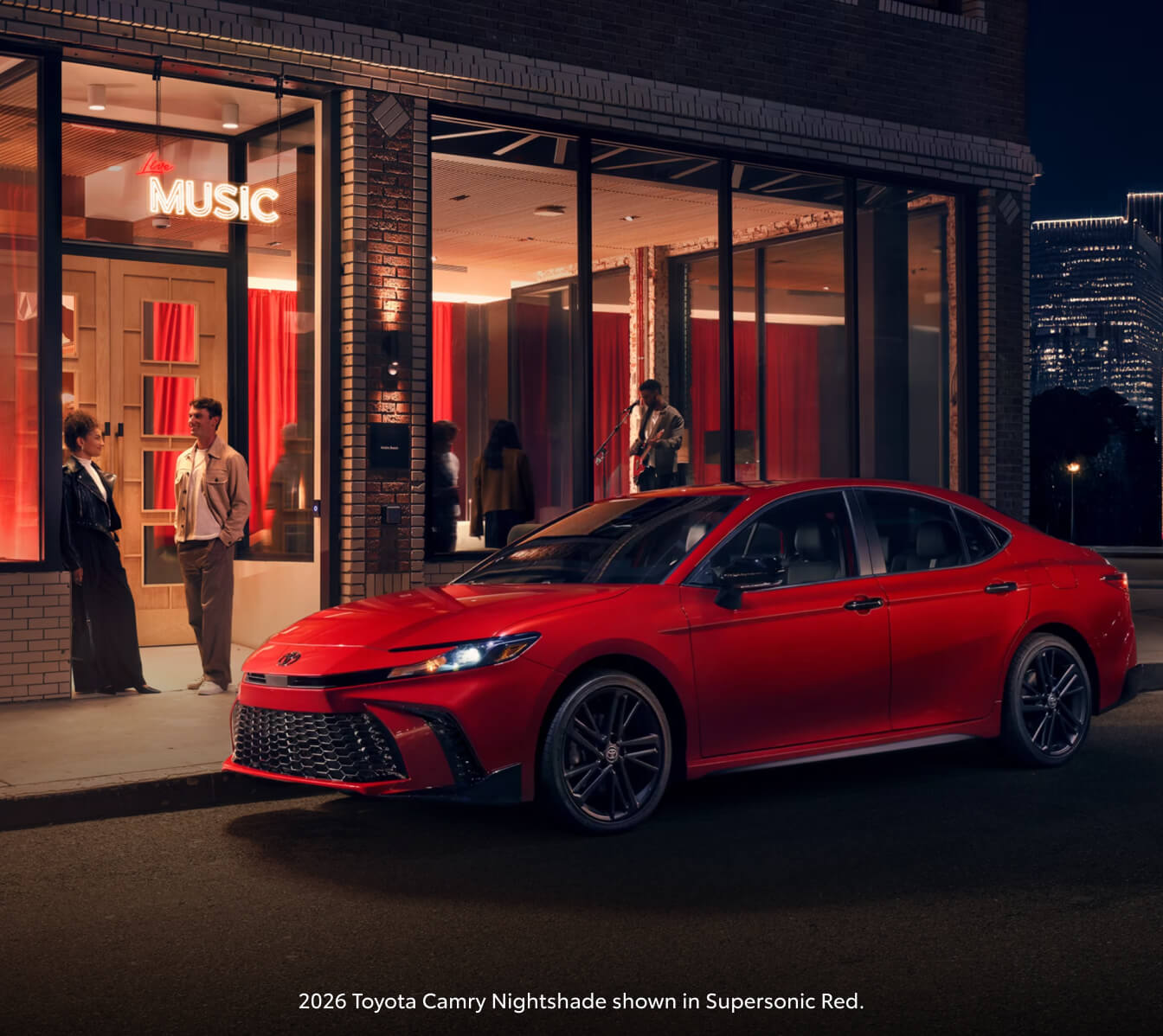 2026 Supersonic Red Toyota Camry Nightshade parked outside a music venue as people gather near the entranc