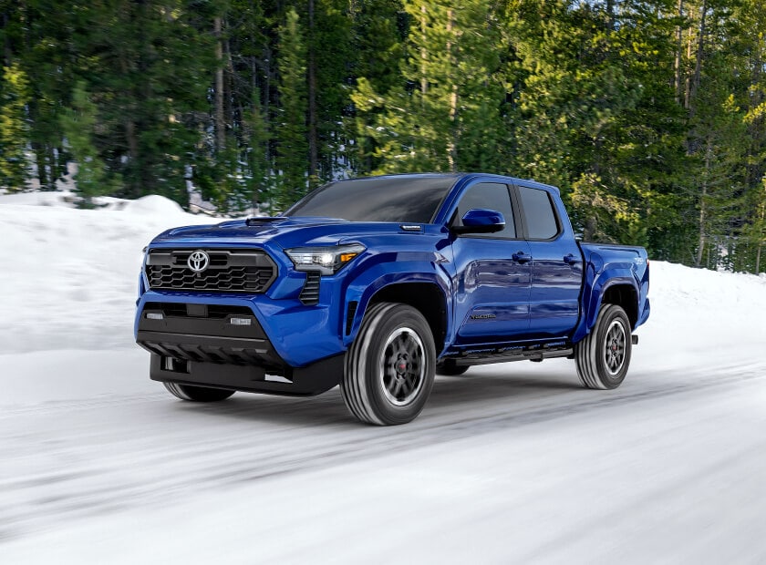 2025 Toyota Tacoma Hybrid TRD Sport in Blue Crush Metallic driving in the snow in front of pine trees