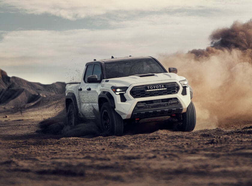 2025 Toyota Tacoma Hybrid TRD Pro in Ice Cap White kicking up dirt while off-roading through muddy terrain