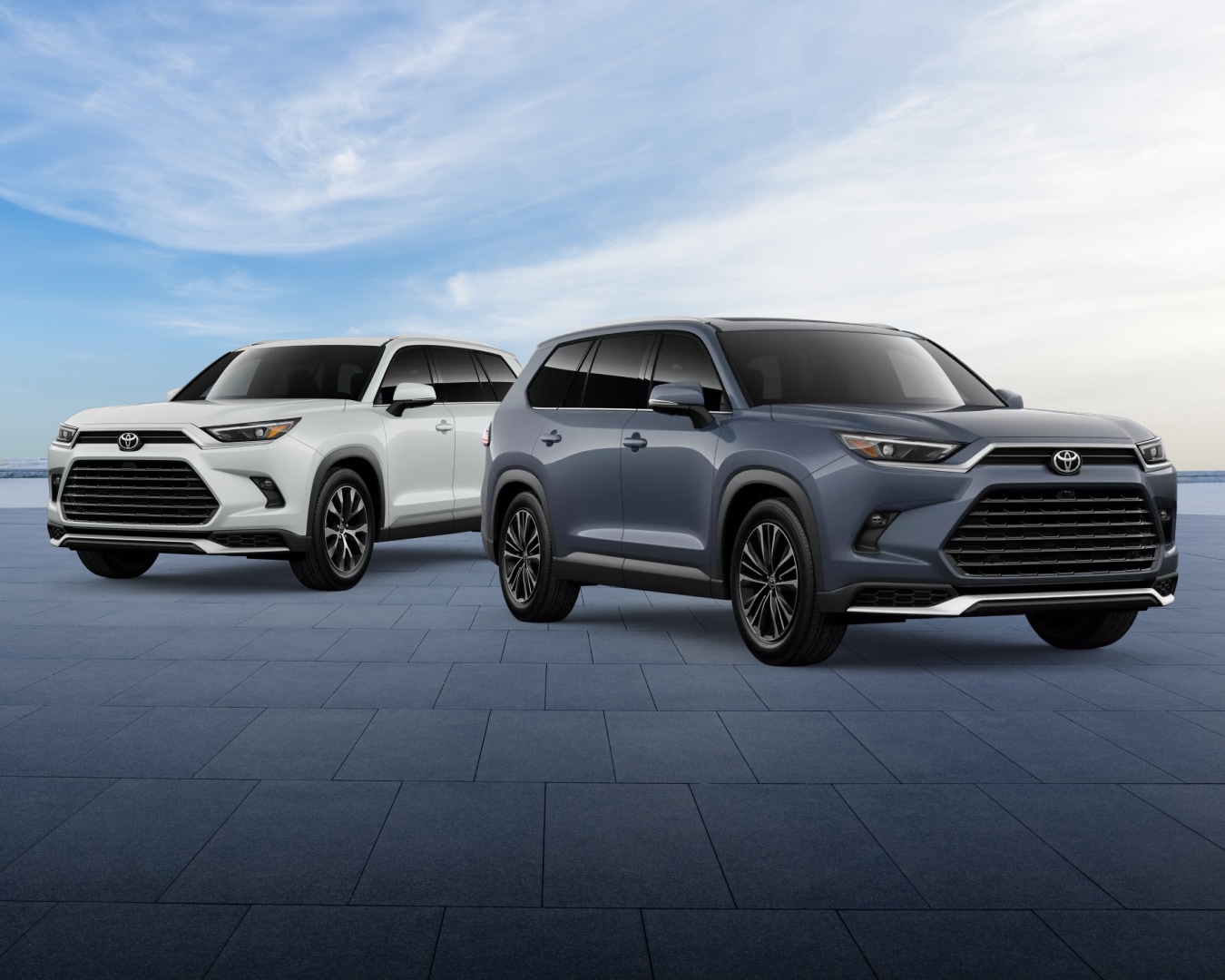 Two new 2026 Toyota grand Highlander Hybrid MAX SUVs parked side-by-side, one in white and on in blue