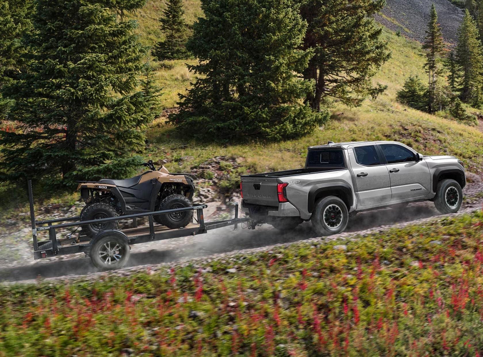 Toyota Tacoma TRD Off-Road in Celestial Silver Metallic towing a trailer and a quad uphill in the forest