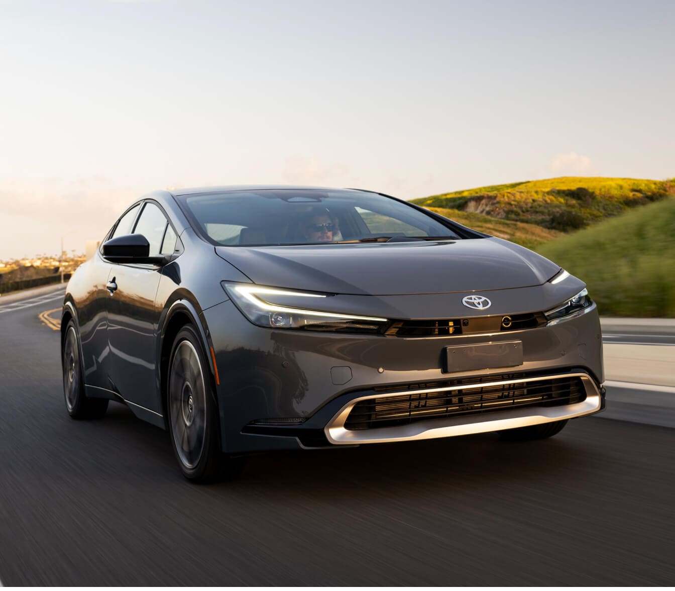 Toyota Prius Limited driving on a winding paved road next to green hills.