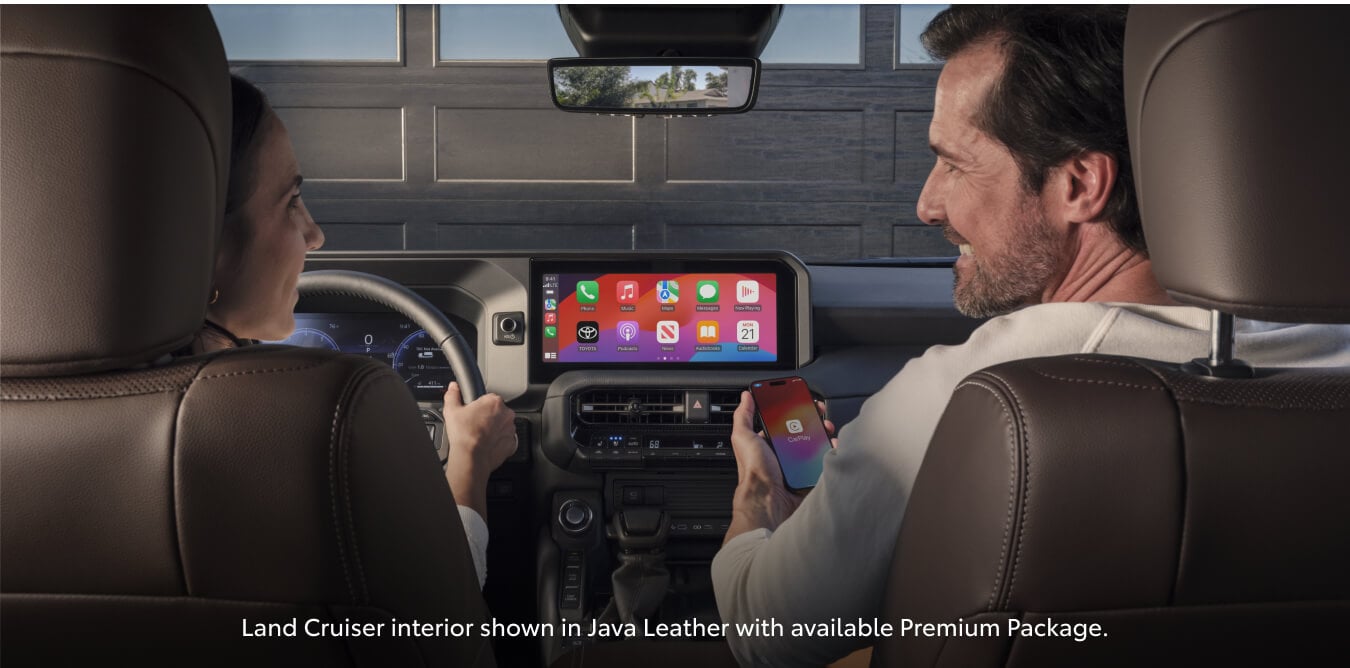 Rear interior view of a Toyota Land Cruiser Premium Java Leather showing passengers using Apple CarPlay.