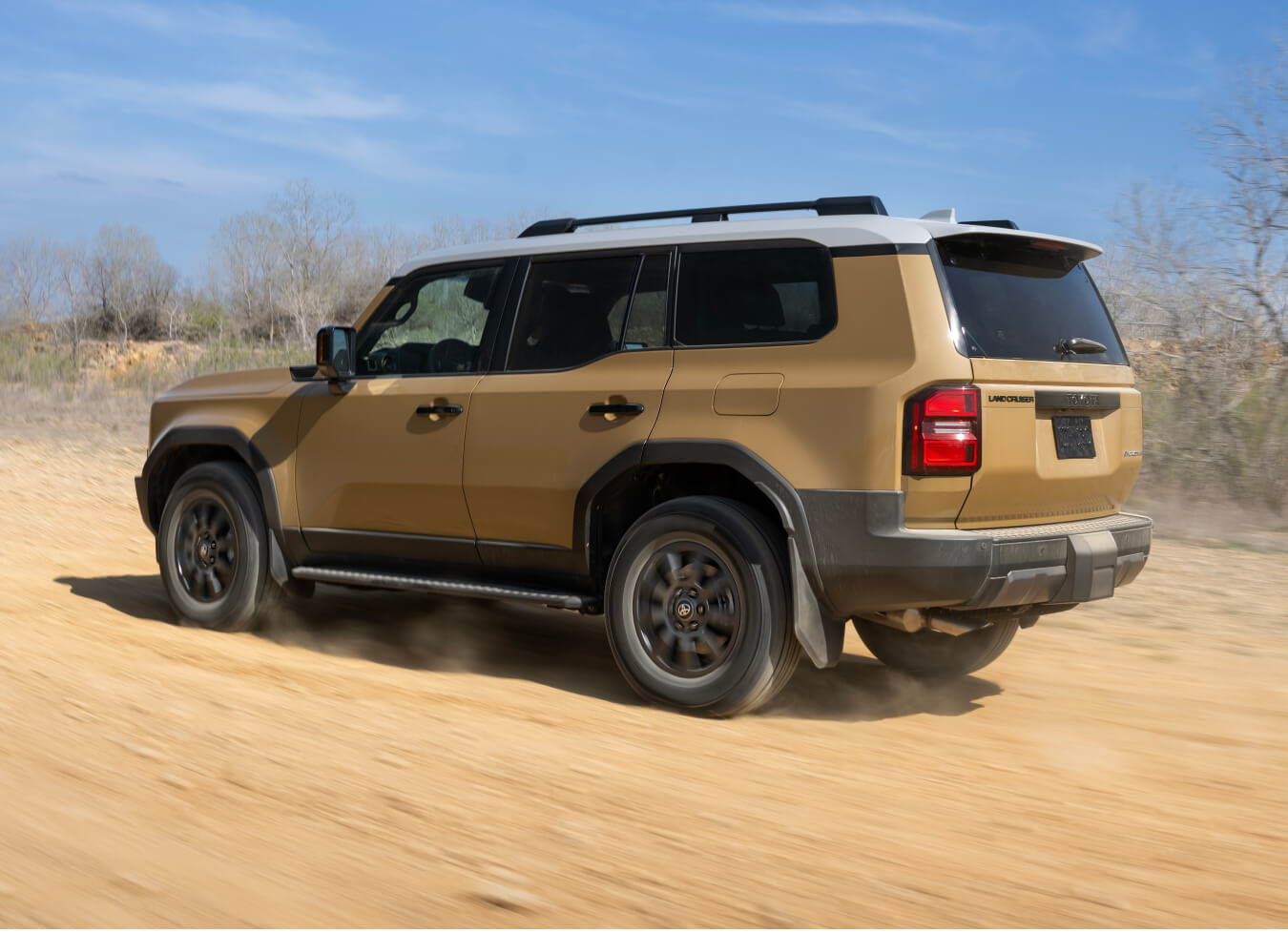 Rear three-quarter view of a Toyota Land Cruiser in Trail Dust on an unpaved country trail.