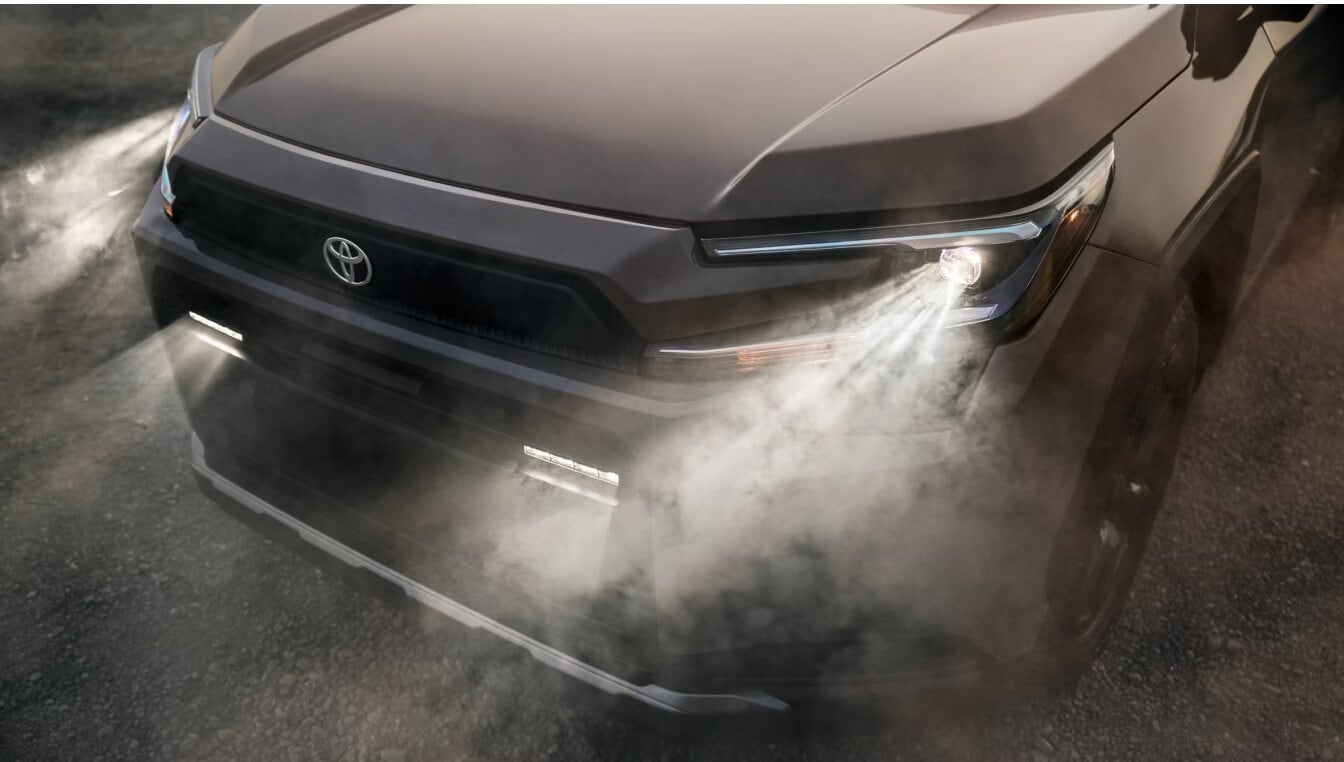Toyota RAV4 Plug-In Hybrid Woodland Edition exterior in Urban Rock showing a close-up front view displaying illuminated LED headlights in heavy fog.