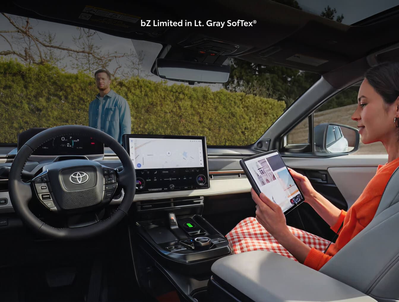 A woman sitting in the passenger seat of a 2026 Toyota bZ looking at a tablet