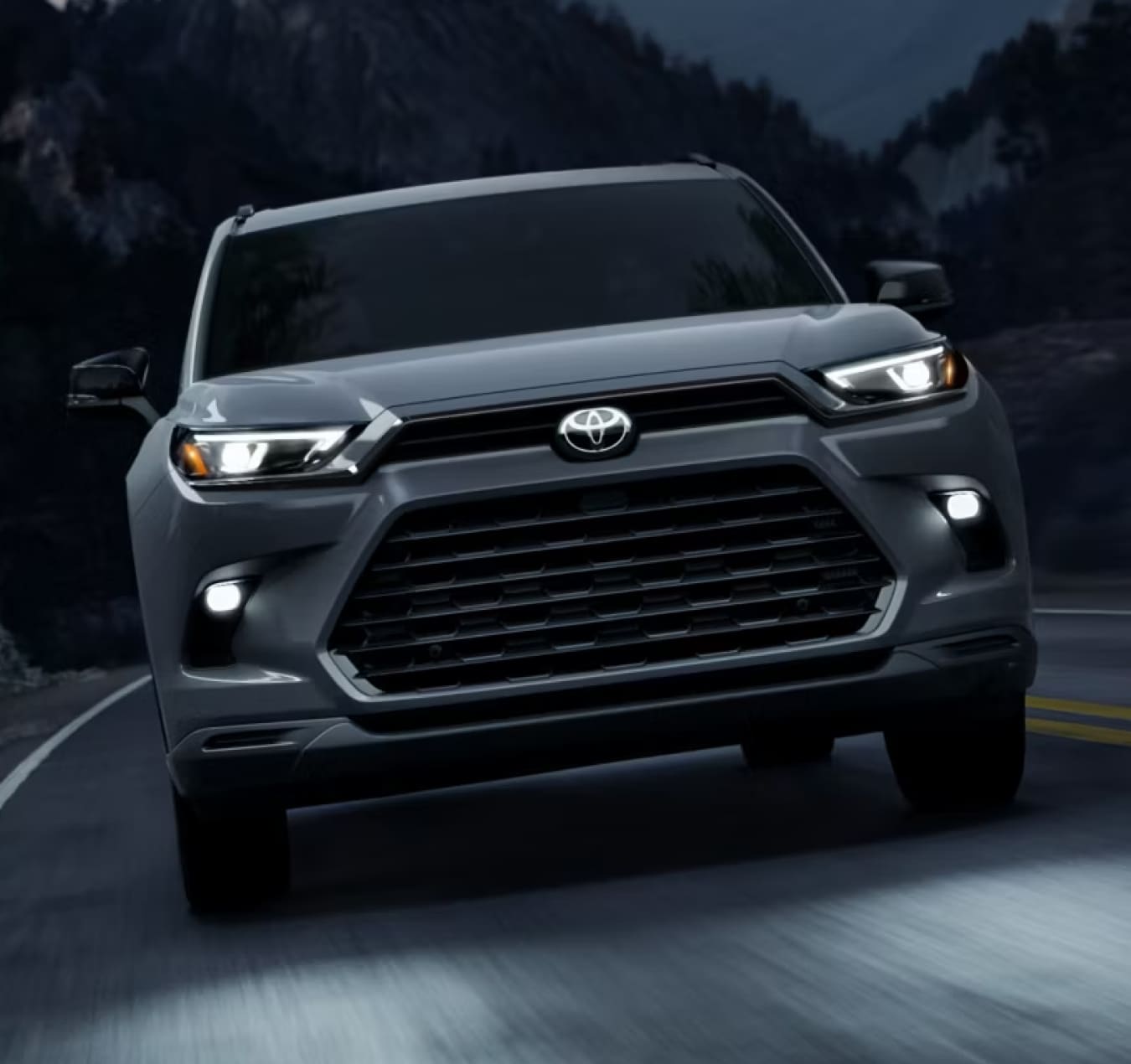 Front view of a 2026 Toyota Grand Highlander Hybrid Nightshade in Cement driving at night