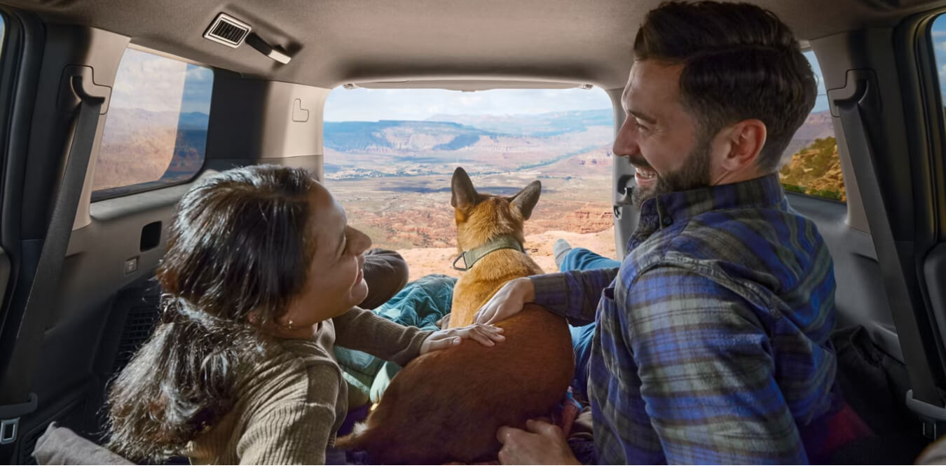 Interior cargo view of a Toyota Land Cruiser in Java Leather with a couple and their dog looking out.