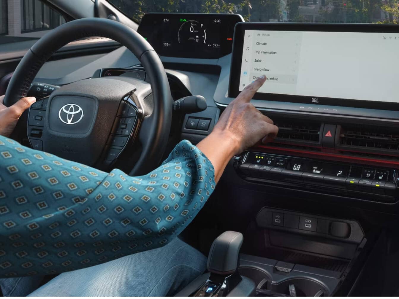 Toyota Prius Prime XSE driver using the multimedia touchscreen during a daytime drive.