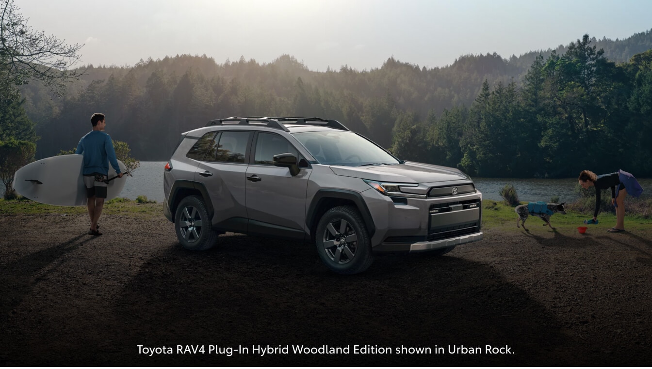 Toyota RAV4 Plug-In Hybrid Woodland Edition shown in Urban Rock showing front three-quarters view parked near a lake.