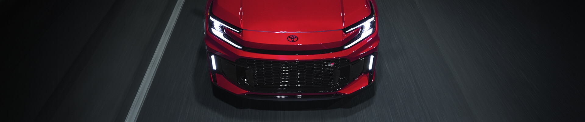 Overhead top-down motion shot of an Supersonic Red Toyota RAV4 Plug-in Hybrid GR Sport speeding along a dark road.
