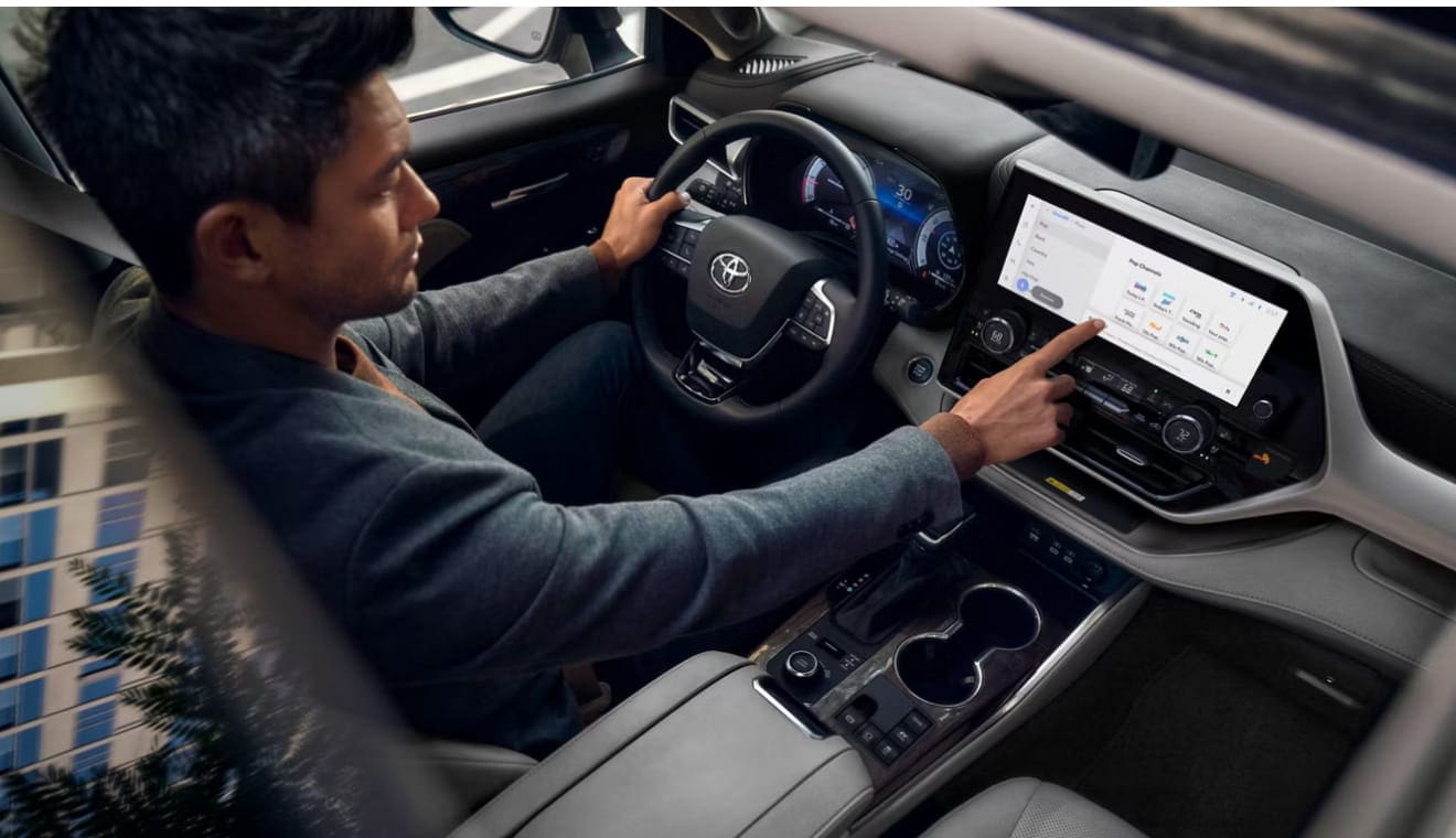 A driver using the infotainment touchscreen inside a new Toyota Highlander.
