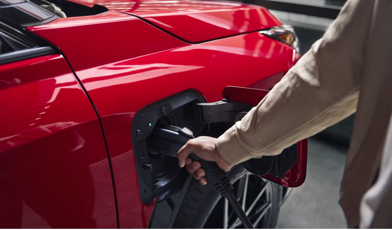 Close-up view of a hand plugging a Level 2 charging cable into a Supersonic Red Toyota RAV4 Plug-in Hybrid GR Sport.
