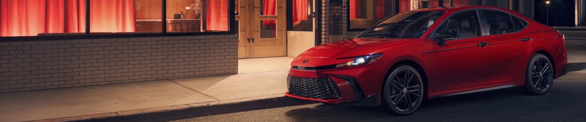New Toyota Camry Nightshade in Supersonic Red parked outside of a music venue