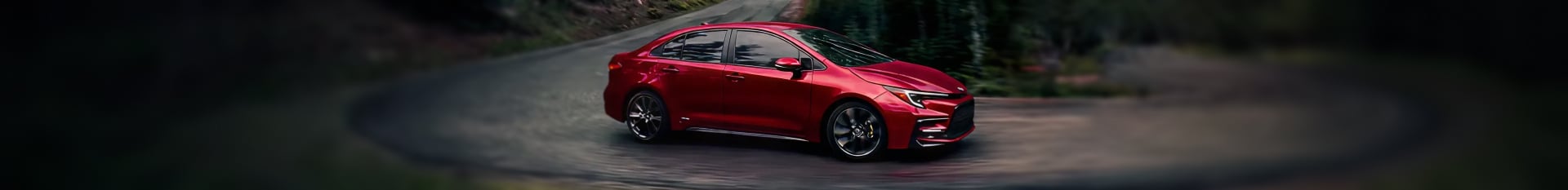 2026 Toyota Corolla Hybrid SE in Ruby Flare Pearl driving down a windy road with a forest green backdropE