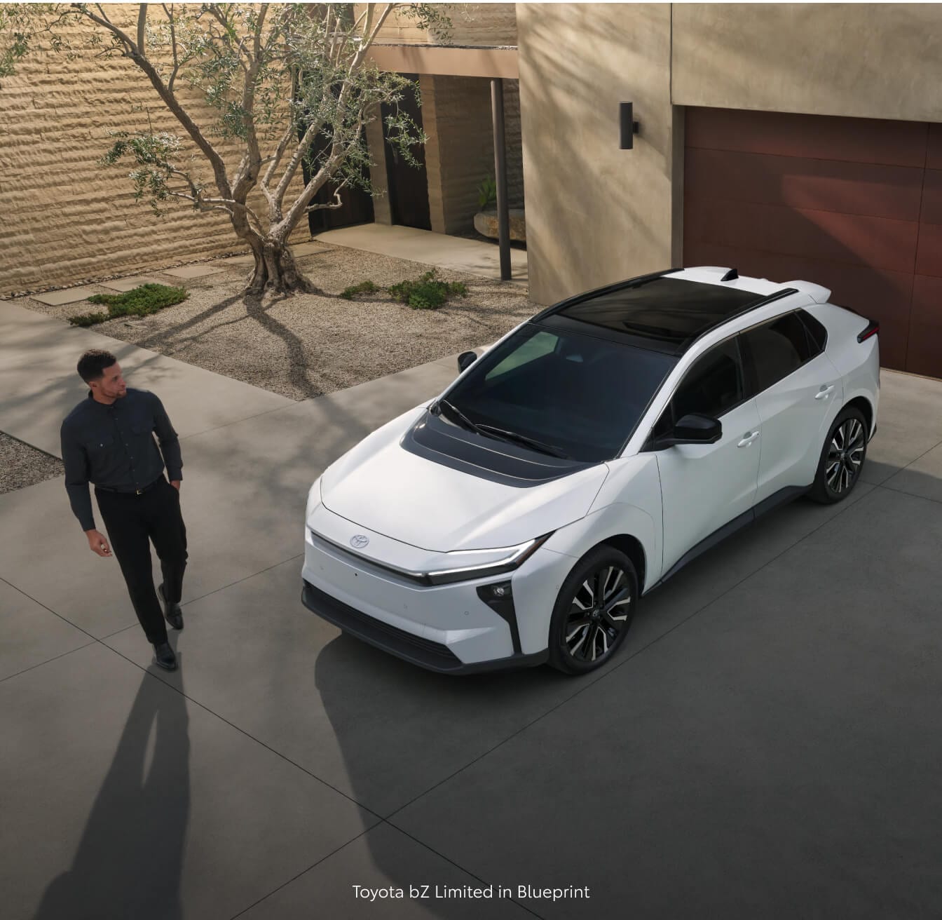 High angle view of a 26 Toyota bZ Limited in Wind Chill Pearl parked as a man walks toward in front a luxury house.