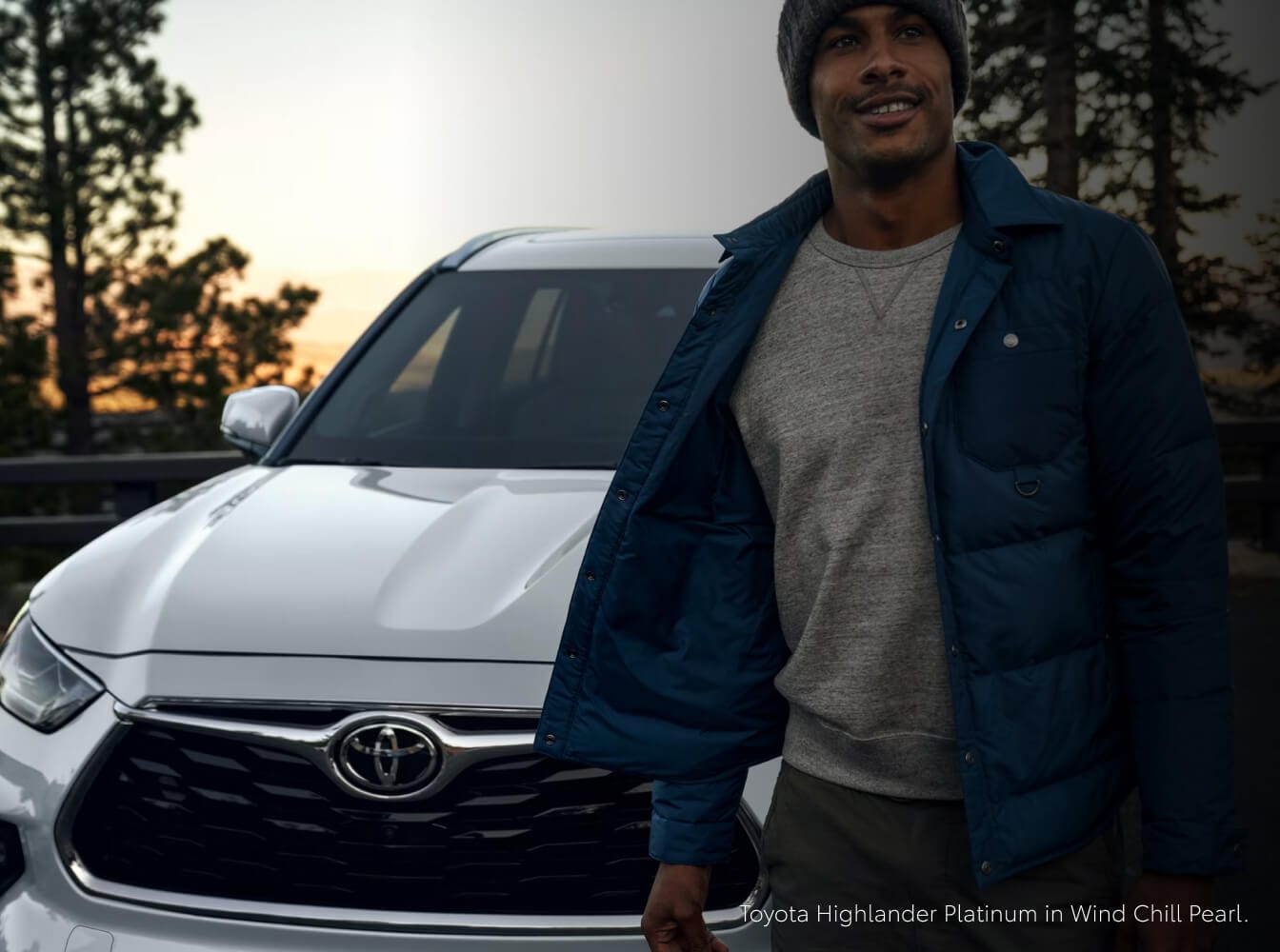 Front view of a 26 Toyota Highlander Platinum in Wind Chill Pearl with a man standing ahead.