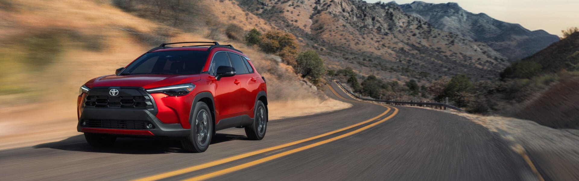 2026 Toyota Crolla Cross in Soul Red Crystal driving on the highway through an arid region