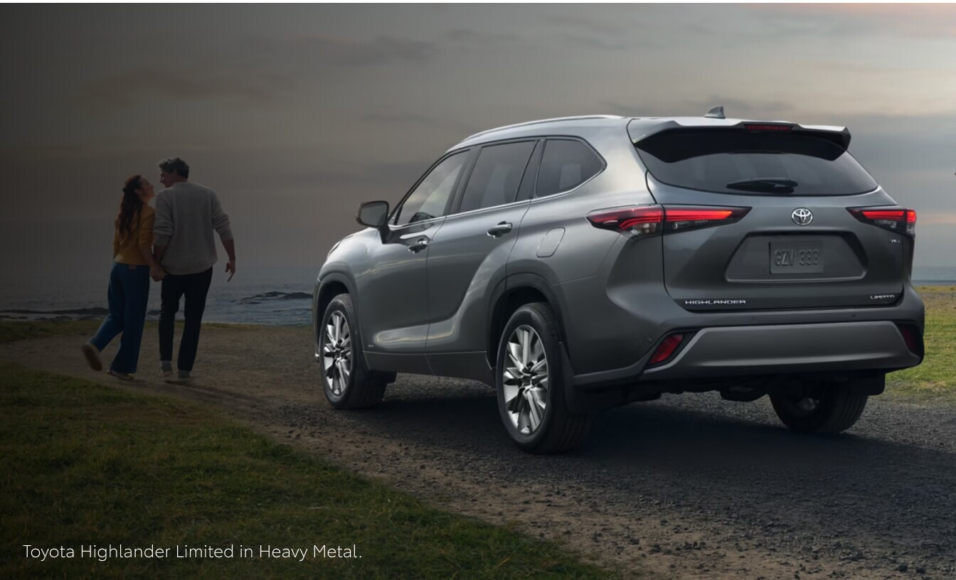 Rear quarter view of a 26 Toyota Highlander Limited in Heavy Metal parked as a couple walks by the coast.