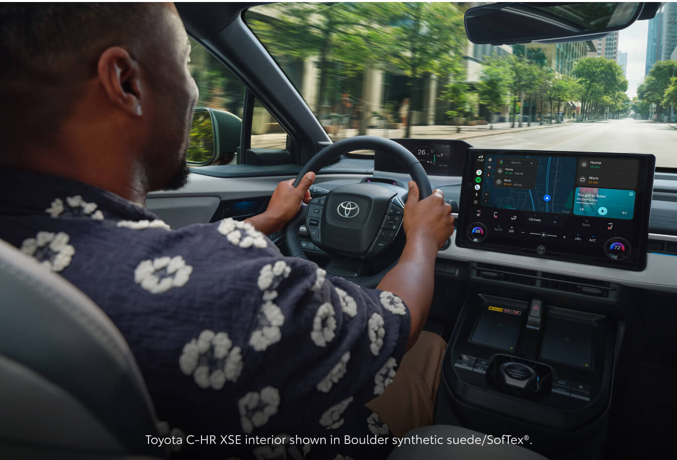 Over-the-shoulder view of a man driving a 2026 Toyota C-HR XSE showing the Boulder synthetic suede/SofTex.