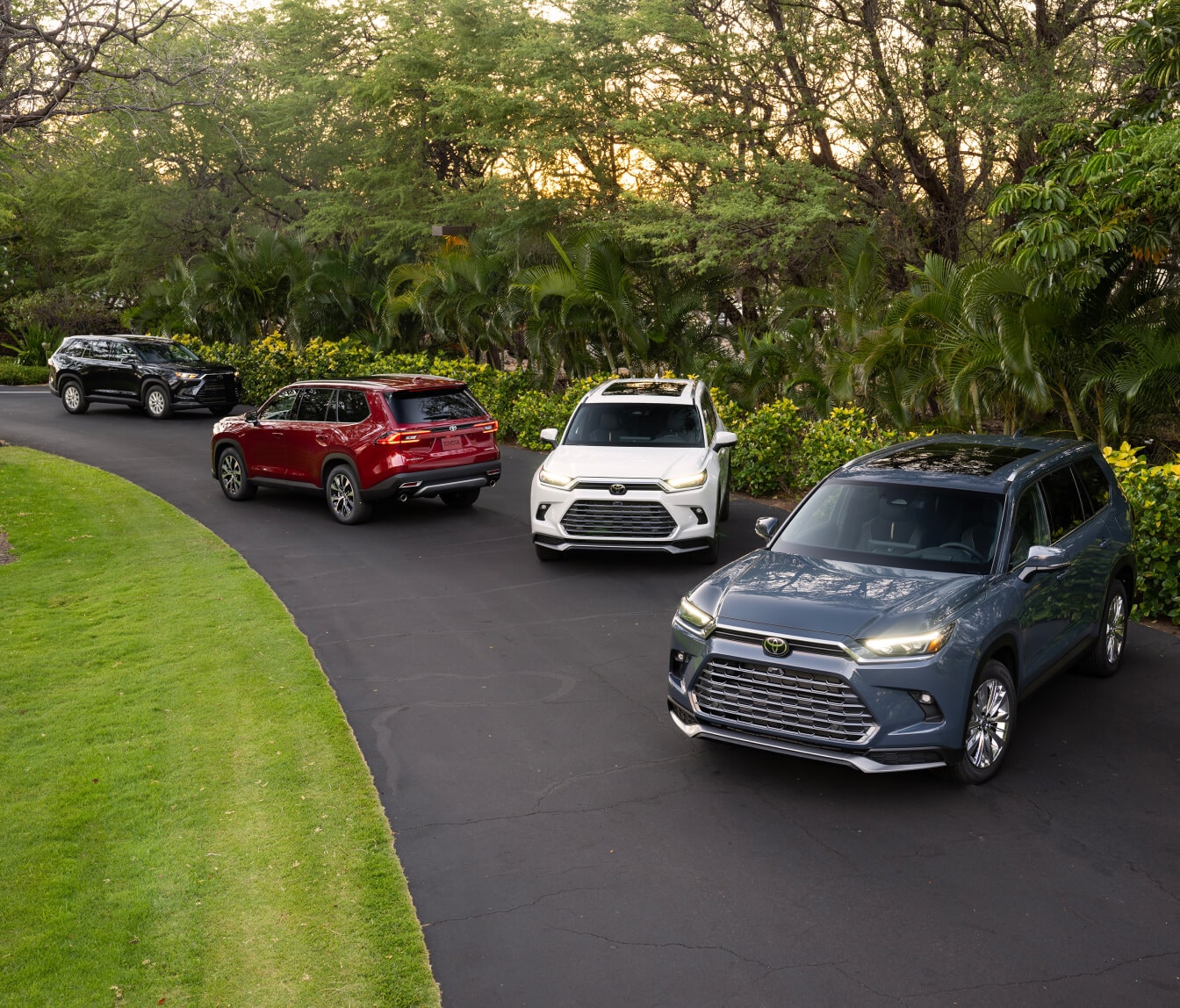 High-angle view of four 2026 Toyota Grand Highlander SUVs in various colors on an asphalt driveway.