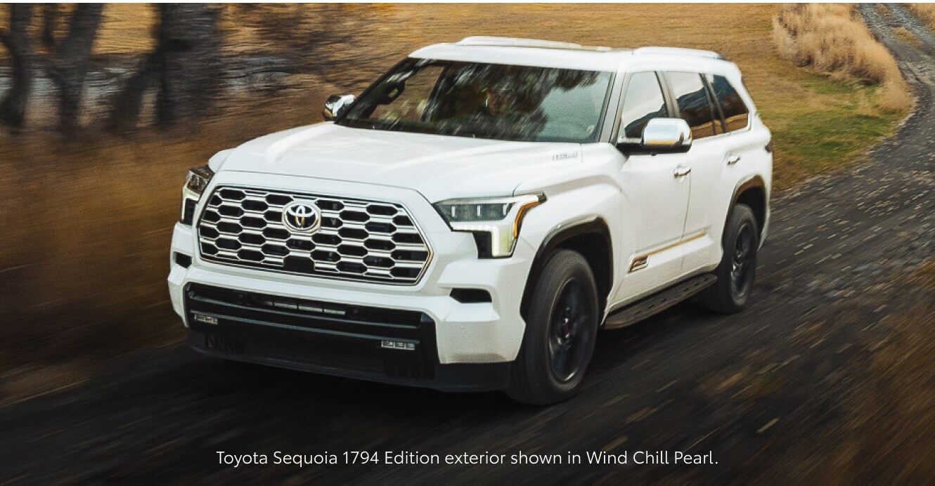 Front-three-quarter view of a 2026 White Toyota Sequoia 1794 Edition driving down a country road.