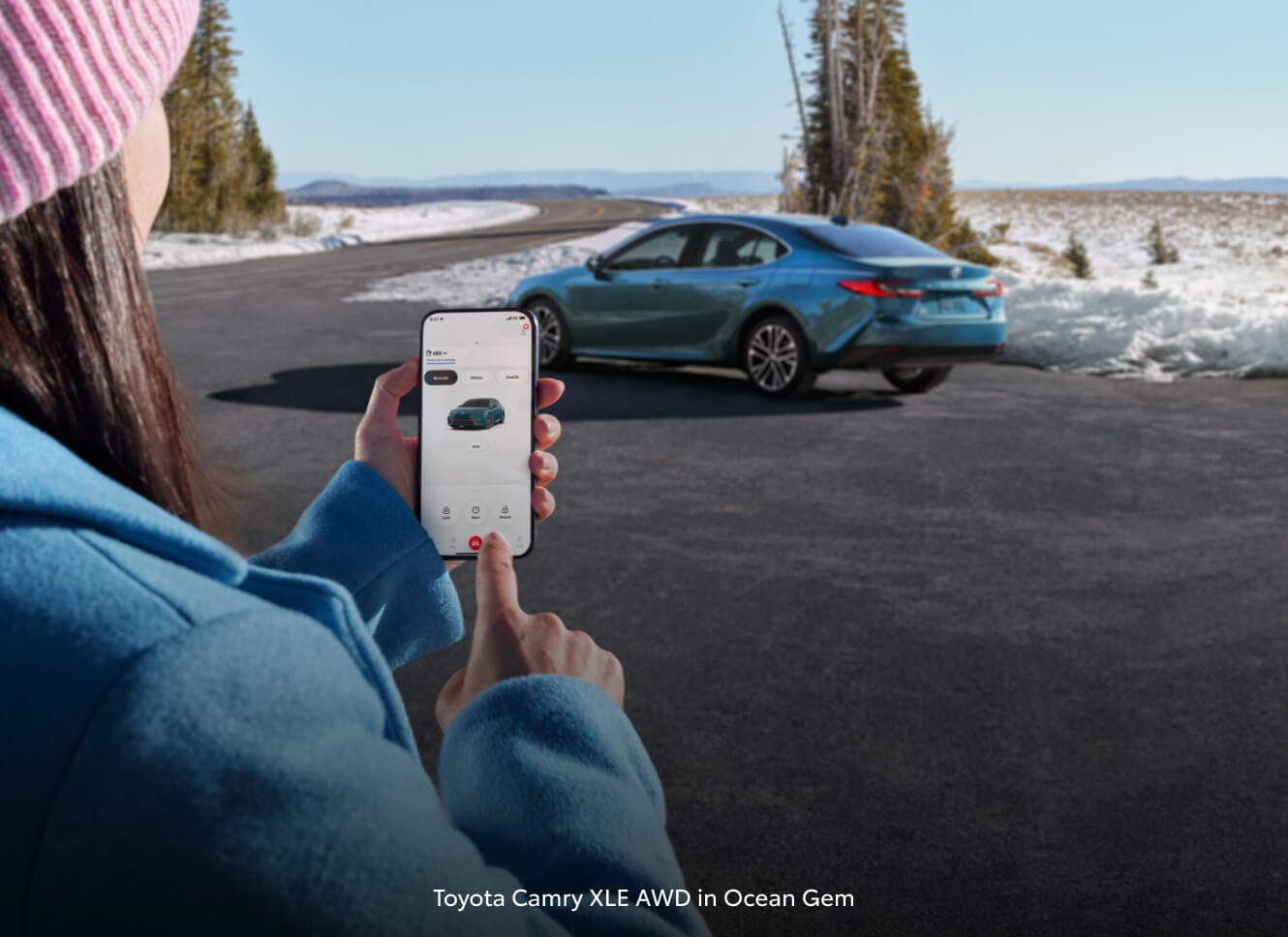 A woman looking up Toyota Camry info on her phone with the real Toyota Camry in the background