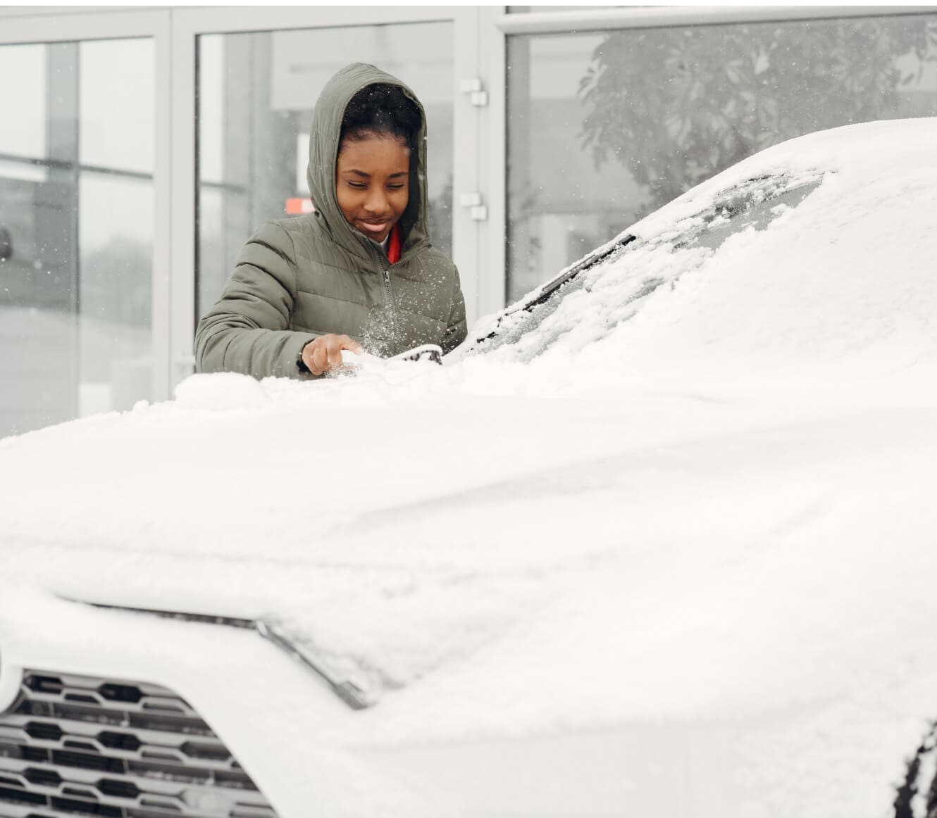 Toyota RAV4 Hybrid XLE in Super White covered in snow with a scraper on building background.