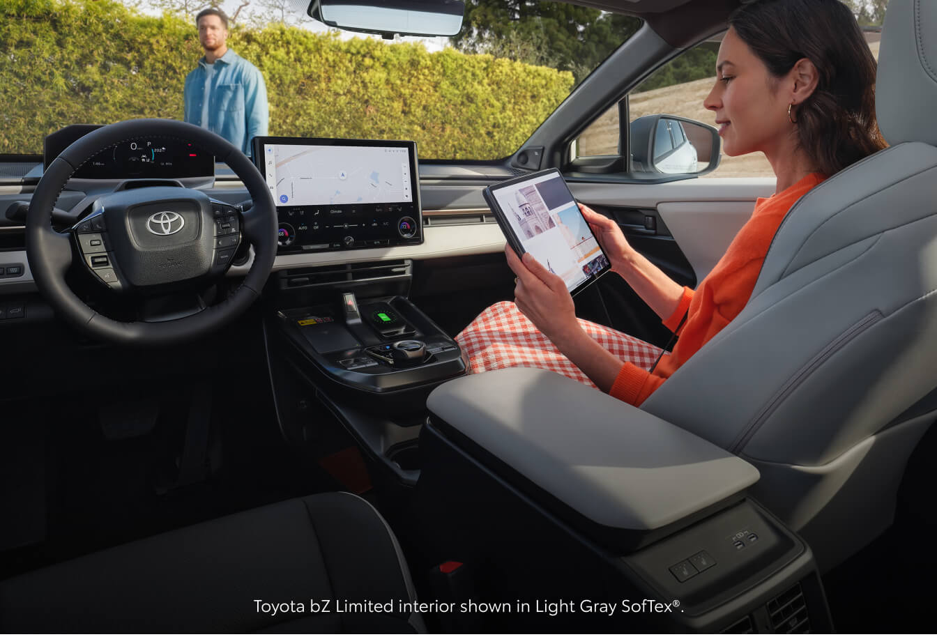 Interior cockpit view of a 2026 Toyota bZ Limited as a woman sits in the Light Gray SofTex passenger seat holding a tablet.