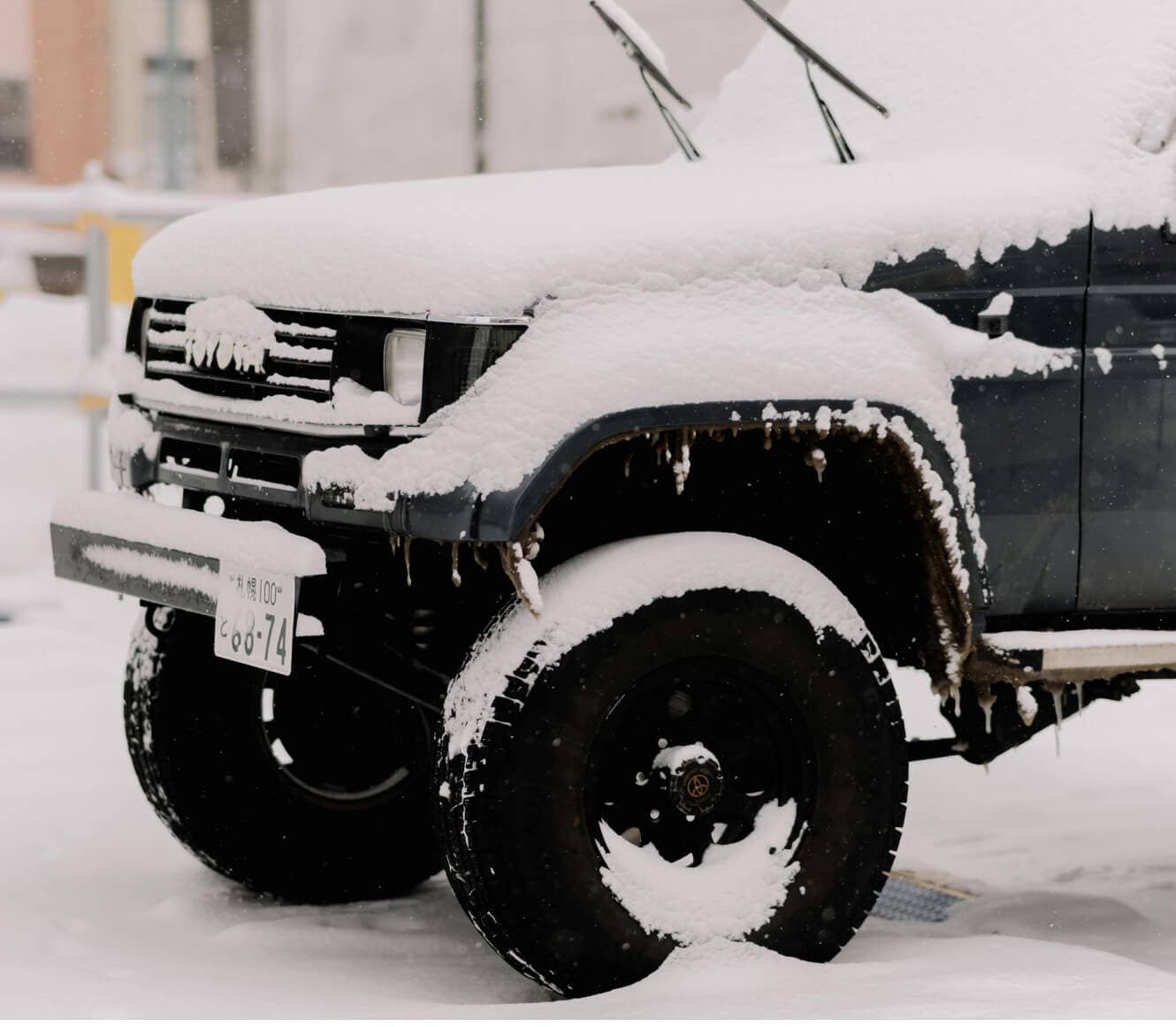 Toyota Land Cruiser Prado EX Wide in Dark Green Mica covered in heavy snow on winter street.