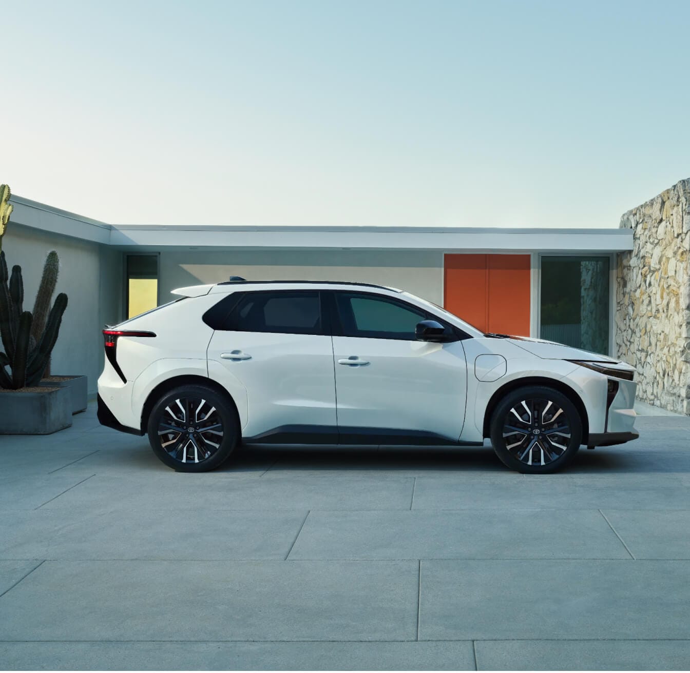 Side profile view of a 26 Toyota bZ Limited in Wind Chill Pearl parked in front of a minimalist home.