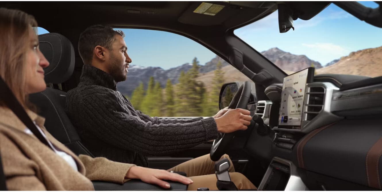 Interior profile view of a 2026 Toyota Sequoia Platinum showing a couple driving past a mountain path.