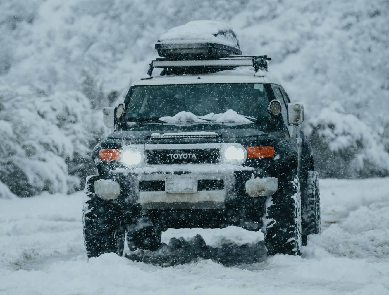 Toyota FJ Cruiser Trail Teams Ultimate Edition in Heritage Blue with roof cargo box driving on snowy road.