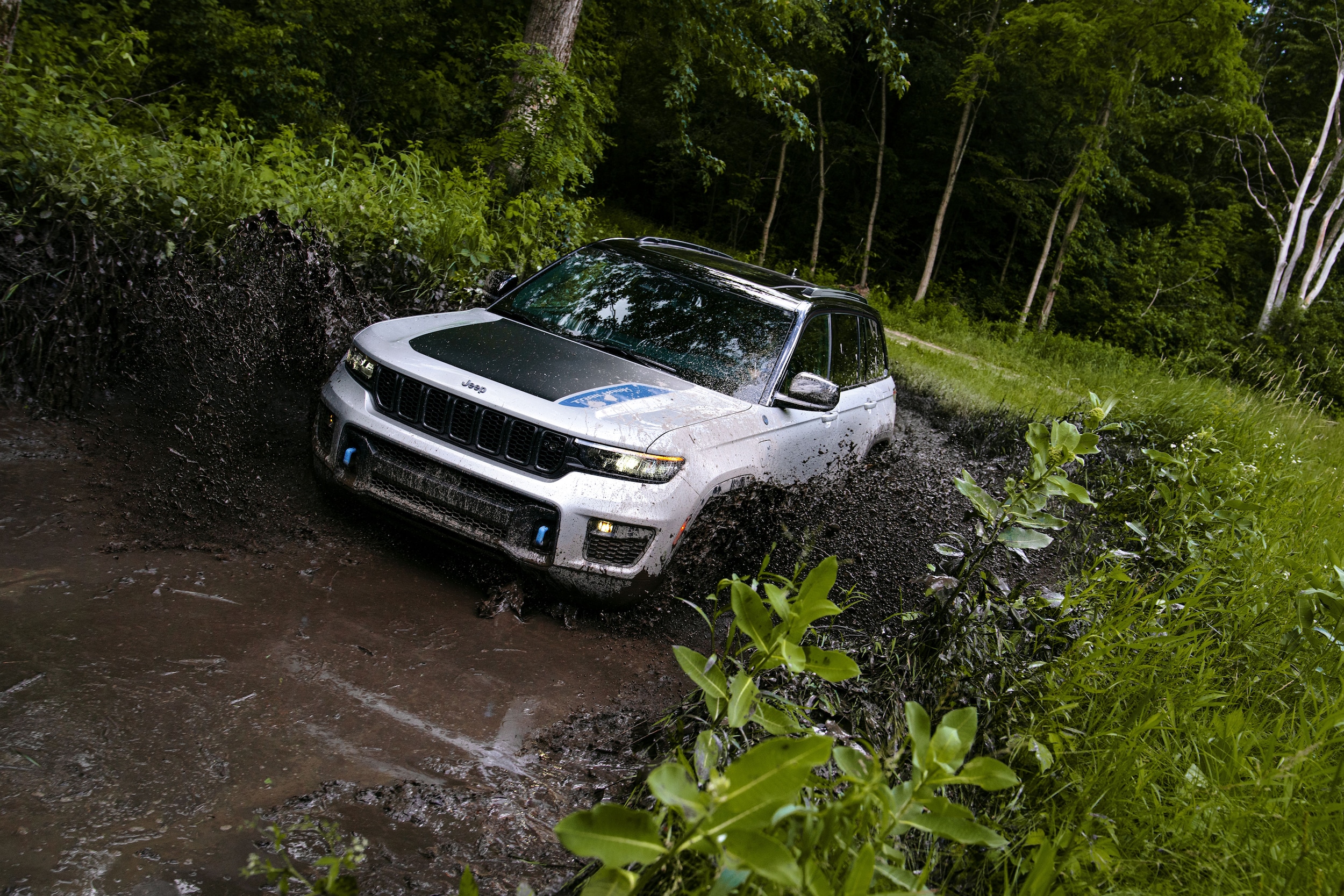 White Jeep Grand Cherokee 4xe driving through water and mud