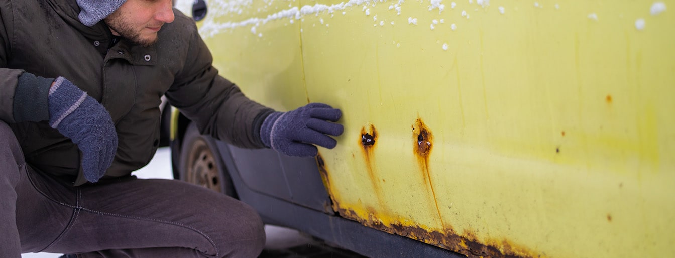 man shows rust on his vehicle in the snow