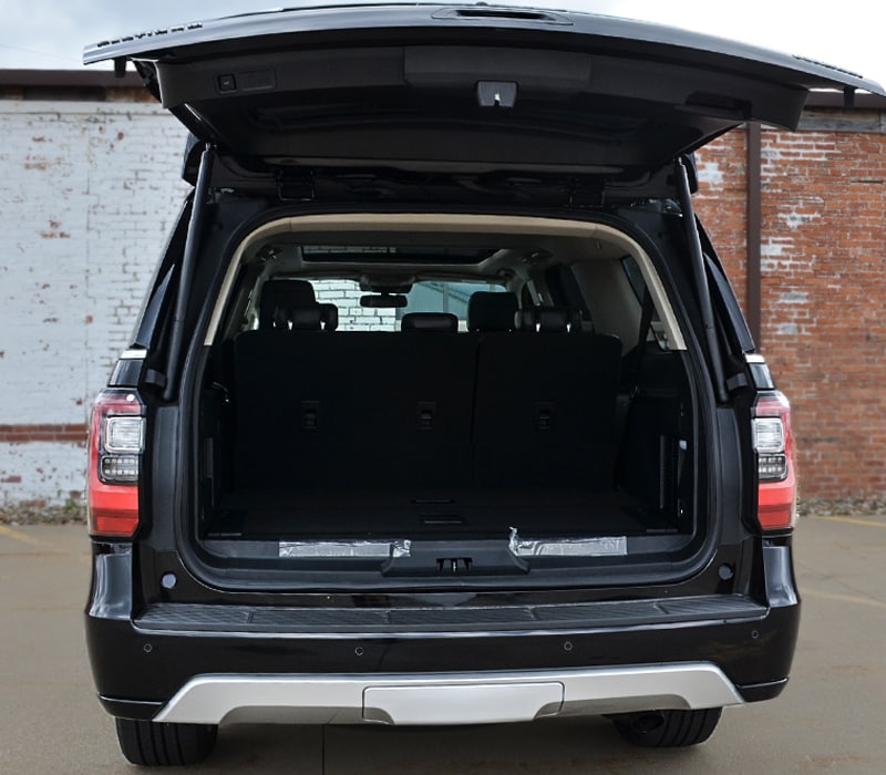 2019 black Ford Expedition rear tailgate opened parked next to brick building