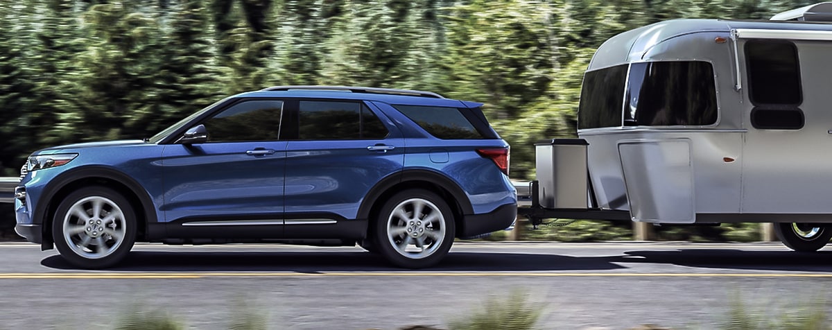 2020 blue Ford Explorer driving through a wooded area towing a trailer